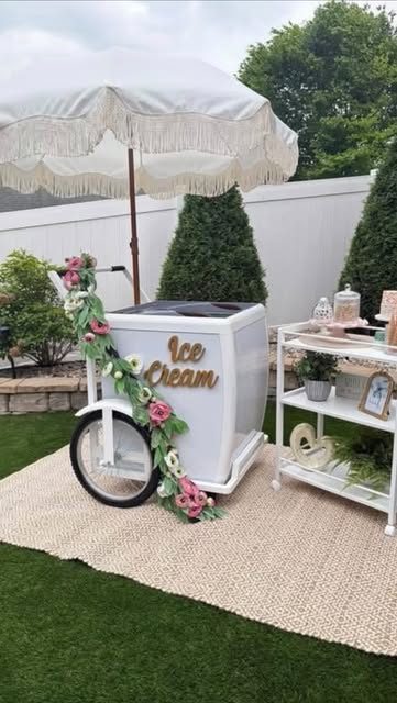 The Belle, BooGi Bliss’s white vintage ice cream cart with a fringed umbrella and floral garland, set up on a lawn